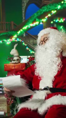 Noel Baba 'nın dikey videosu çocukların mektuplarını okurken uykuya dalıyor. Etrafı tatil malzemeleriyle çevrili. Çocuklara Noel dilekleri listesi okurken uyuyakalan yaşlı bir adam, kamera A