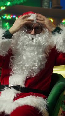 Noel Baba kılığında, sahte sakal, kırmızı ceket ve beyaz ponpon şapkalı bir şovmen portresi. Noel karakterini canlandıran adamın görüntüsü aynaya bakıyor, gözlükleri ayarlıyor.