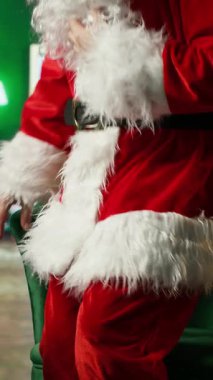 Dikey video Şaşkın Noel Baba hediye kutusunu Noel süsleme odasında bulduğuna şaşırdı. Noel Baba 'yı oynayan yaşlı adam, Noel mucizesi olan hediyeyi masada görünce hayrete düştü.