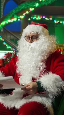 Noel Baba gibi giyinmiş gülümseyen bir adamın dikey video portresi yaramaz ya da iyi el sallayan çocukların listesini yapıyor. Neşeli insan çocukları selamlıyor, oyuncakları dağıtmaya hazırlanıyor, kamera A