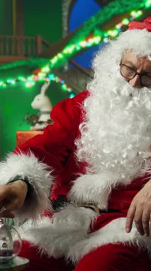 Noel Baba Noel Baba 'nın Noel küreleriyle süslediği dikey video atölyesini ziyaret eden ailelere hazırlıyor. Bayram havası için odada peri masalı süslemeleri yapan kostümlü yaşlı adam, kamera A