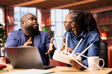 Sinirli siyah çift uzaktan kontrol sırasında Wi-Fi sinyal kaybına kızıyor, sorunları çözmek ya da bir çözüm bulmak için modemi yeniden başlatmaya çalışıyorlar. Kablosuz yönlendiriciyi hata ayıklama veya hata ayıklama.