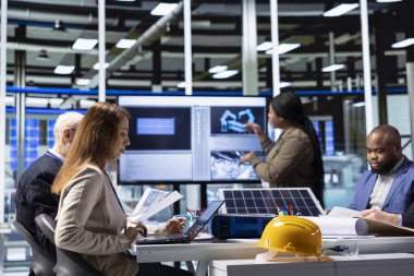 Photovoltaics fabrikası yöneticileri toplantı sırasında teknik verileri analiz ediyorlar, sürdürülebilir üretim ve endüstriyel otomasyon gelişmeleri için stratejik planlama yapıyorlar