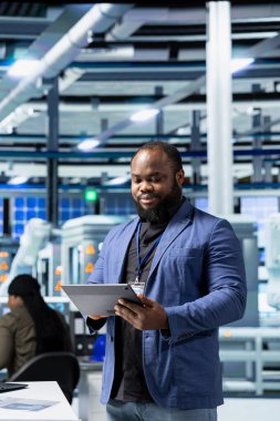 Profesyonel siyah yönetici bir tesiste güneş paneli üretim hattını denetleyerek, kaliteli üretim süreçlerinin kurumsal hedeflere ve yeşil enerji standartlarına ulaşmasını sağlıyor. Sürdürülebilirlik.
