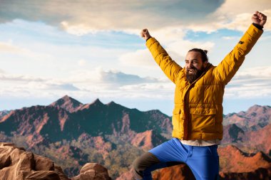 Trekker kollarını dağ sırasının tepesinde heyecan içinde uzatıyor, tırmanma başarısından gurur duyuyor ve tatmin oluyor. Genç yetişkinler azim ve hırslarını sergiler..