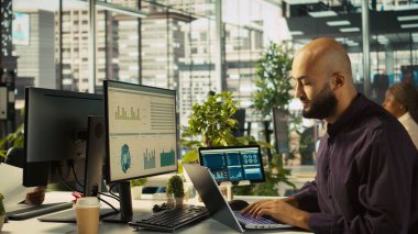 Ofisteki muhasebeci PC 'ye finansal rakamlar girerek iş arkadaşlarına rapor veriyor. İş yerindeki Arap adam bilgisayardaki verileri karşılaştırıyor, çalışma arkadaşlarına belgeler veriyor, kamera B