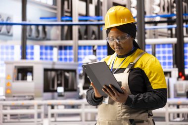 Endüstriyel operasyonları tabletle yöneten Afrikalı Amerikalı kadın verimlilik ve kalite kontrolüne odaklanıyor. Akıllı fabrikadaki makineleri test etmek için dijital cihaz kullanan zenci kadın çalışanlar..