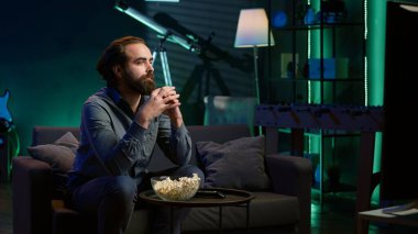 Televizyon ekranında gösterilen ilginç filmle kanepede oturan adam. Neon ışıklı oturma odasında canlı yayın yapan kişi, eğlenceli film sahnesinden büyülenmiş, dikkat çeken, kamera A