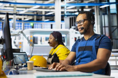 Güneş paneli fabrikasında yardım hattında çalışan siyah müşteri hizmetleri asistanı kulaklıkla çağrılara cevap veriyor, teknik hataları düzeltmek için rehberlik ve yardım sağlıyor. Fabrikadaki genç yardım görevlisi..