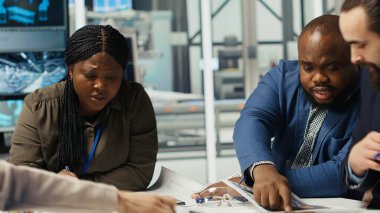 Endüstriyel fabrika yönetimi evrak ve şemaları inceliyor. Fabrika yöneticileri otomasyon teknolojisinin üretime entegrasyonunu tartışmak üzere yatırımcılarla bir araya geldiler.