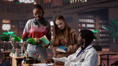 Bir kütüphanedeki çok ırklı öğrenci grubu, tıp kitapları ve materyalleri kullanarak farmakoloji ve mikrobiyoloji alanında uzmanlık kazanmak amacıyla doktorla birlikte bir derse katılıyor. Bilimsel çalışmalar. Kamera B.