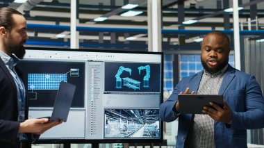 Fabrika yöneticileri yatırımcıların önünde satış yapıyor, üretim hatlarının planlarını gösteriyorlar. Endüstriyel fabrika yapılandırmalarını hissedarlara sunan yönetim, kamera B