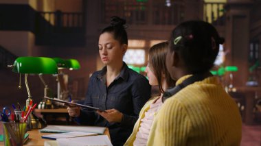 Kütüphanedeki özel dersler sırasında çeşitli öğrencilere eğitim veren kadın akıl hocası, çalışma alanında ödev ve okul projelerine yardımcı oluyor. Rehberlik dersi. Kamera B.