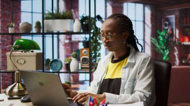 Teleworker masadaki verileri analiz ediyor ve evrak işlerini inceliyor, analitik raporları derliyor. Uzaktan çalışan belgeleri kontrol ediyor, şirket bilgilerini internete yüklemek için dizüstü bilgisayar kullanıyor, kamera A