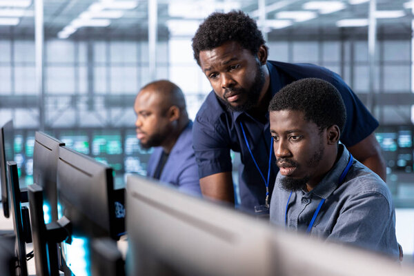 Manager in server hub overseeing workers using computer to find firewall misconfigurations affecting rackmounts. Supervisor checking systems bottlenecks leading to sluggish data transfer rates