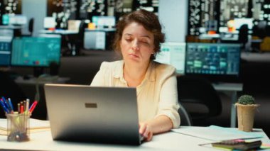 Yönetici iç geçiriyor, saatler sonra gergin ve bunalmış hissediyor, yorgunluk belirtilerine rağmen sınırları zorluyor. İş yerindeki zorluklar, yorgunluk ve cesaretsizlik rahatsızlık veriyor. Kamera B.