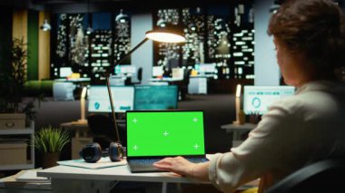 Kadın analist laptopta yeşil ekran kullanıyor ve yeni görevler planlıyor. İş idaresi uzmanı çalışma saatleri dışında masasında çalışıyor. Ofiste yalnız bir kadın. Kamera A.