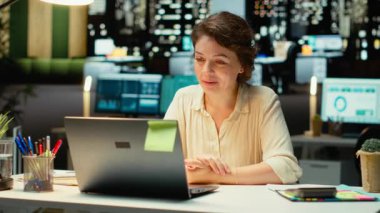 Profesyonel bir kadın telekonferans sırasında dizüstü bilgisayarın önünde oturur ve dijital tartışmalara girer. Katılımcılarla etkileşime girmek, ağ oluşturma oturumunda uyum sağlayabildiğini göstermek. Kamera B.