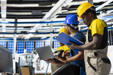 African american team of technicians doing quality control on pc, troubleshooting and fixing technical issues for solar panel production at high tech factory. Coworkers inspecting system.