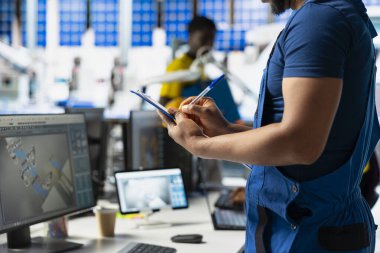 Afrikalı Amerikalı denetçi, dosyalardaki gelişmiş izleme ve üretim araçlarını kullanarak fabrikadaki yenilenebilir enerji ölçümlerini değerlendiriyor. Mühendis güneş enerjisinin doğruluğunu artırıyor.