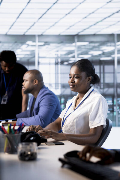 African american technician in data center while running system diagnostic tests and error checking utilities. Woman next to colleagues looking for network issues affecting server performance
