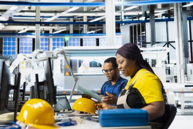 Güneş paneli fabrikasındaki siyah mühendis bilgisayardaki fotovoltaik sistem performansını inceliyor. Endüstriyel üretim tesisinde verimliliği optimize etmek için üretim hattını analiz eden kadın çalışan.