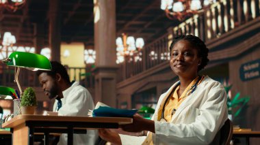 Odaklanmış tıp öğrencisi, önemli bir tıp fakültesi sınavına hazırlanarak farmakoloji üzerine bir ders kitabı okumayı seviyor. Üniversite kütüphanesindeki kadın öğrenci kariyeri için öğreniyor. Kamera B.