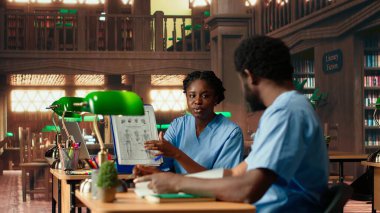 Siyahi tıp fakültesi öğrencileri kütüphanede anatomi kitapları ve ders notları okuyor çalışma grubu öğrenme seansı. İnsanlar tıp kariyeri için sınav hazırlıklarına odaklanıyor. Kamera B.