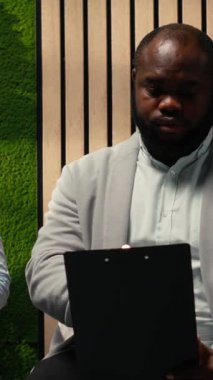 Dikey Video Siyah genç başvuru sahibi HR ofisinde görüşmeye çağrılıyor, koridorda oturuyor ve CV 'deki deneyim sunumunu gözden geçiriyor. İşe alım tartışmasına hazırlanıyorum. Kamera B