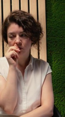 Dikey Videolu Kadın İş Adayı baskı altında sırada bekliyor, tırnaklarını yiyor ve sırada beklerken koridorda gergin davranıyor. Diğer adayların yanında oturuyor. Kamera B.