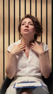 Dikey Videolu Kadın İş Adayı baskı altında sırada bekliyor, tırnaklarını yiyor ve sırada beklerken koridorda gergin davranıyor. Diğer adayların yanında oturuyor. Kamera A.