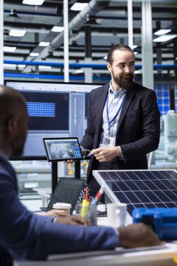 Fotovoltaik fabrika müdürü tablet kullanarak güneş paneli otomasyon stratejileri sunuyor. Güneş panelleri imalat süreçlerini geliştirmenin yollarını yatırımcılara göstermek için aygıt kullanan bitki uzmanı