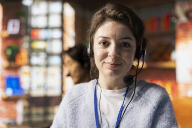 Ofisteki neşeli çağrı merkezi çalışanının portresi müşterilere soruları cevaplayarak, sorunlarını çözerek yardım ediyor. Müşterilerle konuşmak için kulaklık kullanan neşeli müşteri destek çalışanı