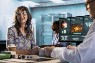 Kıdemli kadın, doktoruyla birlikte teşhis sonuçlarını kabinede değerlendiriyor. Hastasına doğru sonuçları vermek için ileri teknoloji aletleri kullanıyor. Tıp endüstrisinde bakım yönetimi.