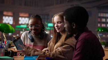 Çok kültürlü öğrenci grubu, kütüphanede notları olan dizüstü bilgisayar ve ders kitaplarını kullanarak bir üniversite dersi için finans projesini tartışıyor. Girişimcilik ve yönetim becerileri. Kamera A.