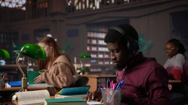 Siyahi adam akademik başarıya odaklanmak için çalışma müziğini kullanıyor, güvenilir kaynaklar bulmak için kampüs üniversite veritabanına başvuruyor. Erkek üniversite öğrencisi diploma için savaşıyor. Kamera B.