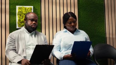 Koridordaki siyah adaylar beklerken doldurulması gereken dosyalar, devam eden işe alım süreci için kayıt formları ve özgeçmiş alıyorlar. İşleme katılıp başlamayı bekliyor. Kamera B.