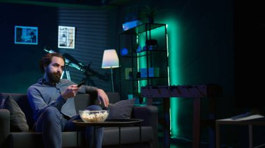 Kanepede oturan bir adam televizyon kanalında film seyrediyor, işten izin almanın tadını çıkarıyor. Televizyondaki kanalı değiştirmek için uzaktan kumandayı kullanan kişi, kamera B