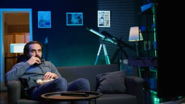 Televizyondaki gerilim filmlerine inanmayan, ağzı patlamış mısırla dolu bir adam. VOD kanalında gerilimli film izleyen şaşkın insan, şaşırmış durumda.