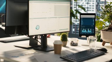 Parlak ofis ortamındaki cihazlarda analitik veri göstergelerine sahip modern çalışma alanı. Finansal istatistik grafikleri saksı bitkilerinin yanında olan masadaki bilgisayar ekranı, dümen aşağı