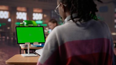 Üniversite öğrencisi kampüs kütüphanesindeki izole edilmiş kroma anahtar ekrana bakıyor, bir okul projesi üzerinde çalışıyor ve akademik uzmanlık kitaplarından bilgi topluyor. Araştırıyorum. Kamera A.