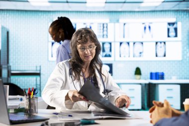 Genel pratisyen hekim, kabinede kıdemli bir hastayla röntgen testi sonuçlarını okuyor ve muayene sırasında tarama yorumu yapıyor. Sağlık hizmetleri sağlık sigortası kapsamında.