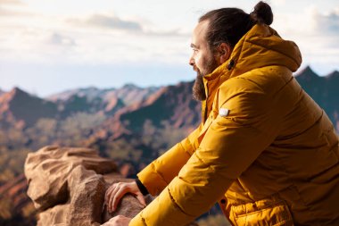 Genç maceraperest tepeden manzaralı bir dağ manzarasına bakarak doğanın yalnızlığını ve temiz havasını kucaklıyor. Farkındalık ve keşif hissi..