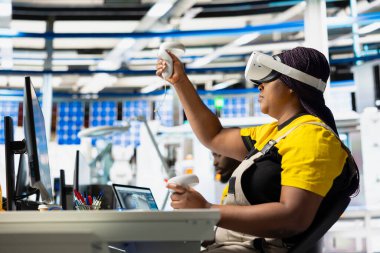 Dijital güneş pillerini monte etmek için VR gözlükleri kullanan fotovoltaik fabrikası mühendisi, yazılım ve robotik kollarla güneş panelleri yerleştiriyor. Sanal gerçekliği kullanarak güneş santralini inceleyen kadın işçi..