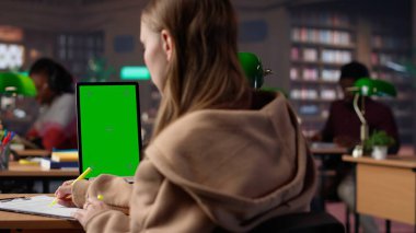 Genç kız öğrenci, yaklaşan sınavları için kütüphanede yeşil ekranla ders çalışıyor. Üniversite gazetesi için akademik bilgiler topluyor. Lisans diploması araştırması. Kamera A.