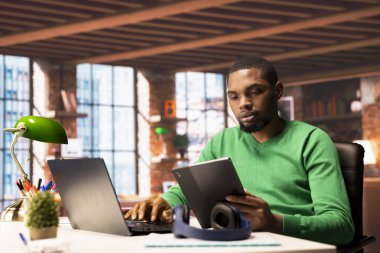 Merkez ofisteki adam internette laptop ve tablet üzerinde geziniyor, internette bilgi araştırıyor. Çalışmalarla ilgili verileri bulmak için dijital aygıtlar üzerinde arama motoru kullanan bir telgraf çalışanı