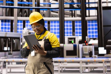 Fabrika müdürü endüstriyel ortamdaki üretim süreçlerini denetlemek için tablet kullanıyor. Siyah kadın yazılım uzmanı depo iş akışını optimize etmek için sistem güncellemeleri uyguluyor.