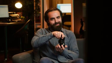 Memlekette oyun oynayan ve boş zamanların tadını çıkaran neşeli bir oyuncu. Neon ışıklı oturma odasında kanepede oturan gülümseyen adam, konsolda video oyunu oynayacağı için heyecanlı, yoğun bir iş gününden sonra dinleniyor, kamera A