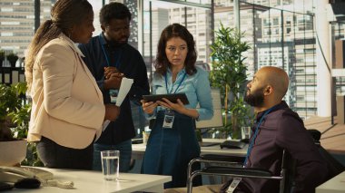 Belden aşağısı felçli çalışanlar ve ofisteki meslektaşları beyin fırtınası yapıyor, finansal tabloları inceliyor, KPI 'ları analiz ediyor. Belden aşağısı felçli kişi ve iş arkadaşları verileri karşılaştırıyor, kamera B