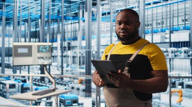 Sanayi 4.0 fotovoltaik fabrikası mühendisi güneş pillerinin enerji üretimini maksimuma çıkarmak için tablet üzerinde yazılım kullanıyor. Güneş panellerini denetleyen Afrikalı Amerikalı adam akıllı fabrika ekipmanları, kamera A